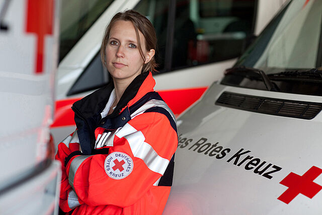 Mitarbeiterin des Rettungsdienstes lehnt sich an einen Rettungswagen.